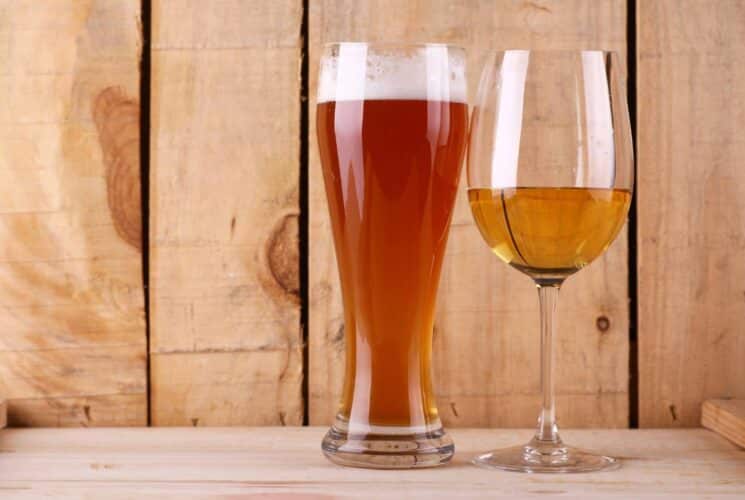 Close up view of beer in a stein glass and wine in wine glass with natural wood in the background