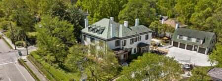 Aerial view of property painted white with brown trim and brown shutters surrounded by large green trees