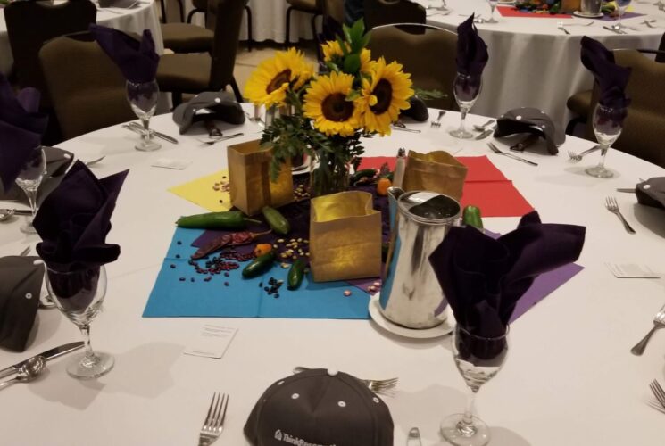 Close up view of round table with white tablecloth and multiple black hats at each place setting