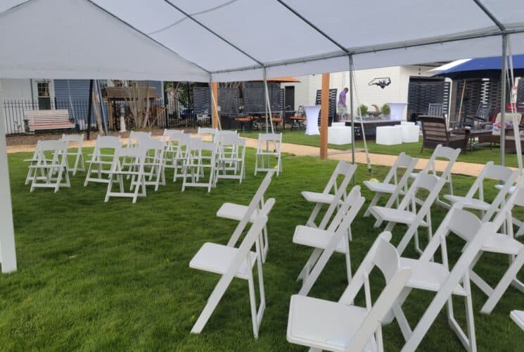 Large white tent set up on green lawn with multiple white chairs set up for an event