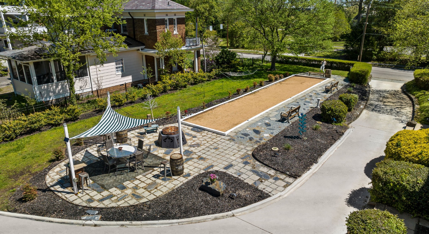 Aerial view of side yard with green grass, bocce court, and patio table under a sun shade