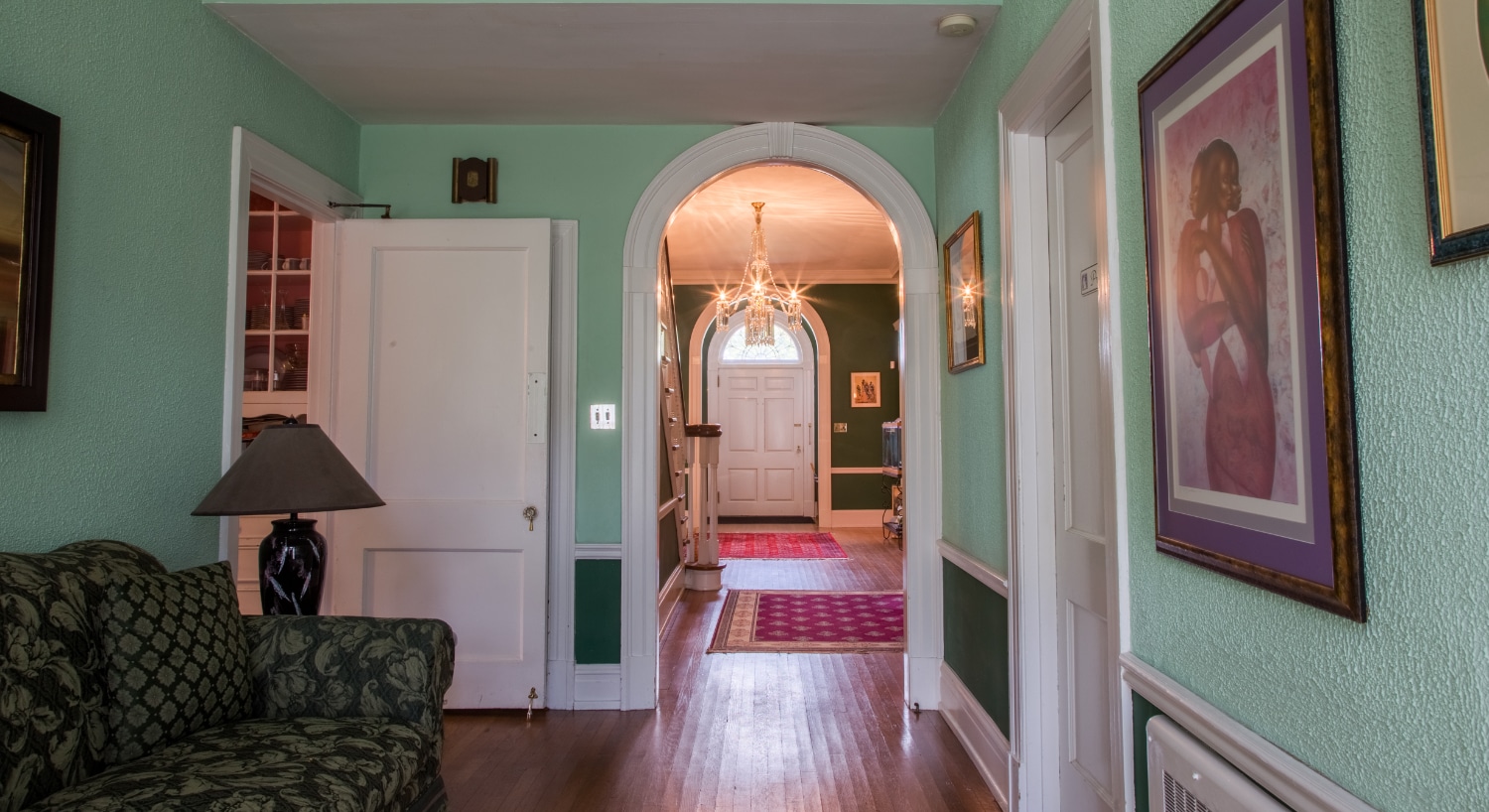 Sitting room with lime green walls, green floral upholstered sofa, and view into foyer with chandelier and staircase to second floor