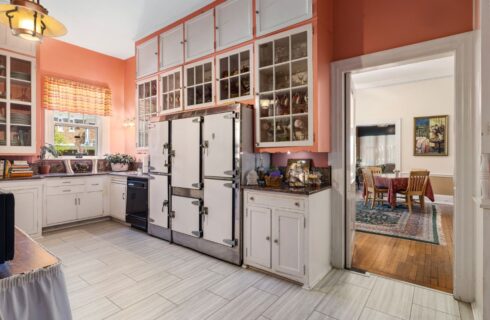 Kitchen with salmon walls, marble tile flooring, white cabinets, and view into dining room