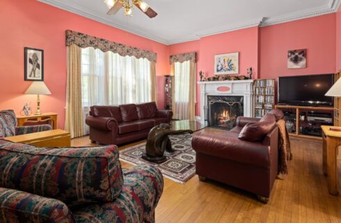 Living room with coral walls, hardwood flooring, brown leather sofas, fireplace, and large windows