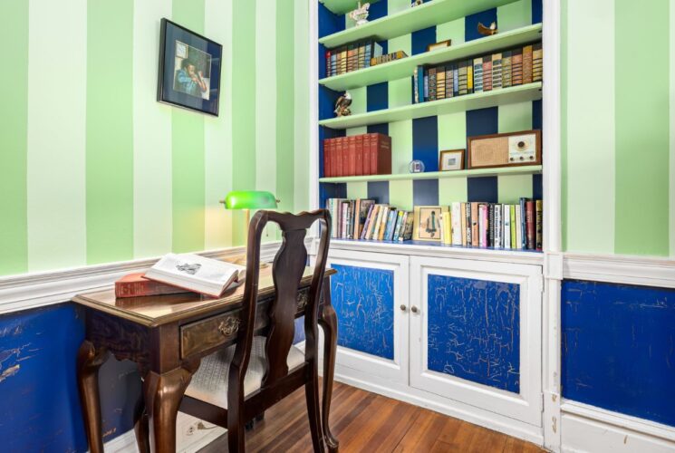 Bedroom area with light green striped walls, blue wainscotting with white trim, built in bookshelves, and antique desk with wooden chair