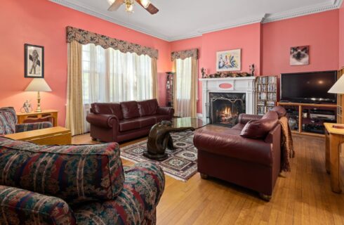 Living room with coral walls, hardwood flooring, brown leather sofas, fireplace, and large windows