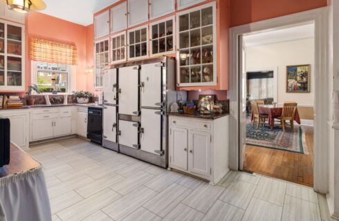 Kitchen with salmon walls, marble tile flooring, white cabinets, and view into dining room