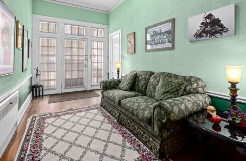 Room with light green walls and dark green wainscotting, hardwood flooring, and green floral upholstered couch, and dark end tables with lamps