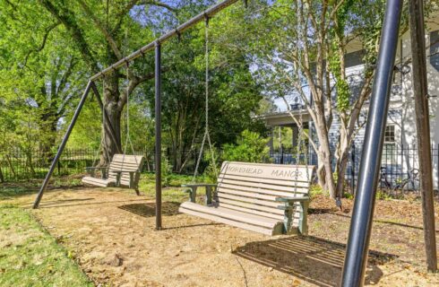 Two wooden bench swing sets surrounded by green grass and large green trees