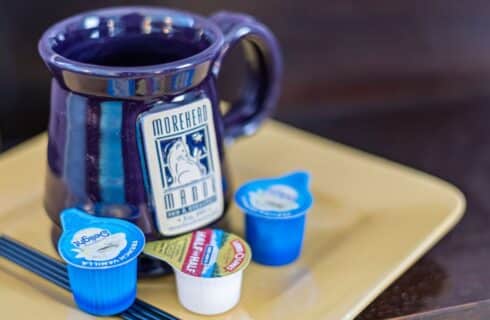 Close up view of purple stoneware mug with Morehead Manor Bed & Breakfast logo sitting on yellow square plate