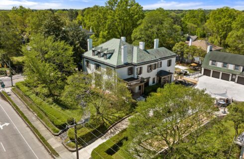 Aerial view of property painted white with brown trim and brown shutters surrounded by large green trees