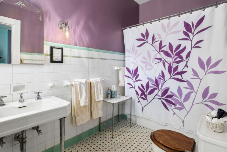 Bathroom with white tile wainscotting and purple walls, white sink, toilet, and tub/shower combo unit