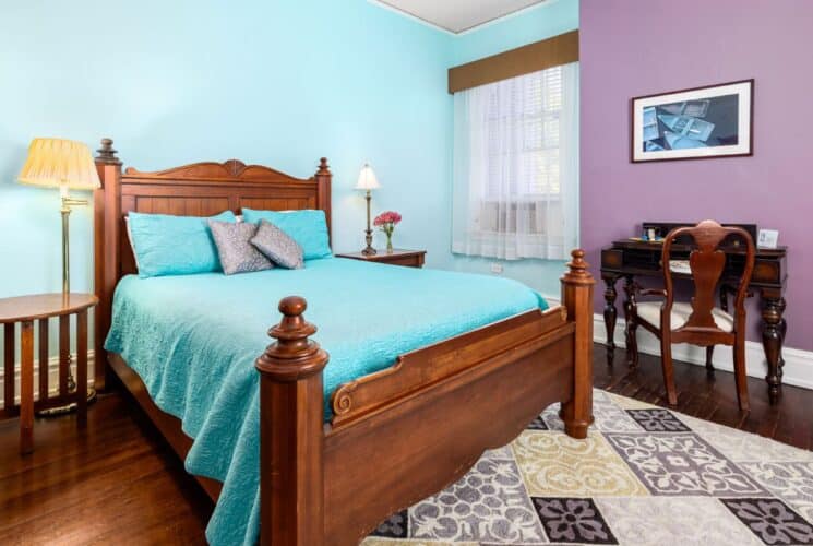 Bedroom with light blue and purple walls, hardwood flooring, wooden bed, turquoise bedding, and dark wooden antique desk