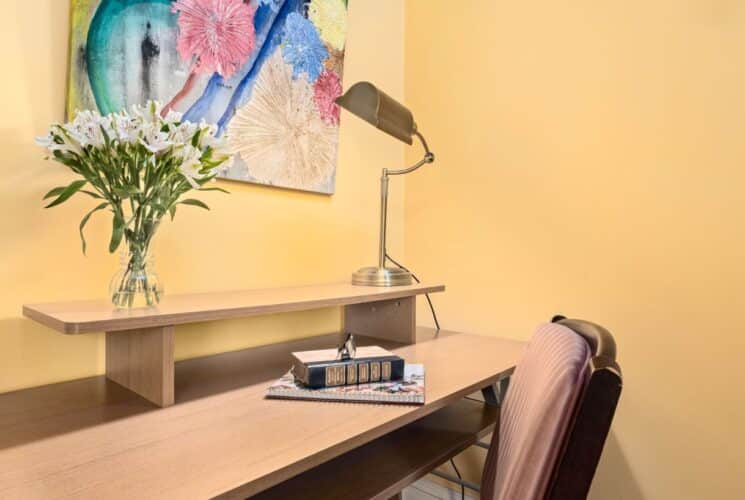 Close up view of light wooden desk, lamp, and chair in bedroom with yellow walls