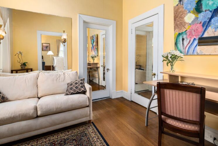 Bedroom sitting area with yellow walls, hardwood flooring, cream upholstered love seat, and light colored desk with chair