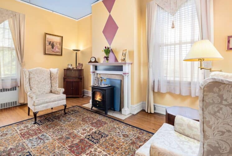 Bedroom sitting area with yellow walls, hardwood flooring, cream floral upholstered armchairs, and fireplace