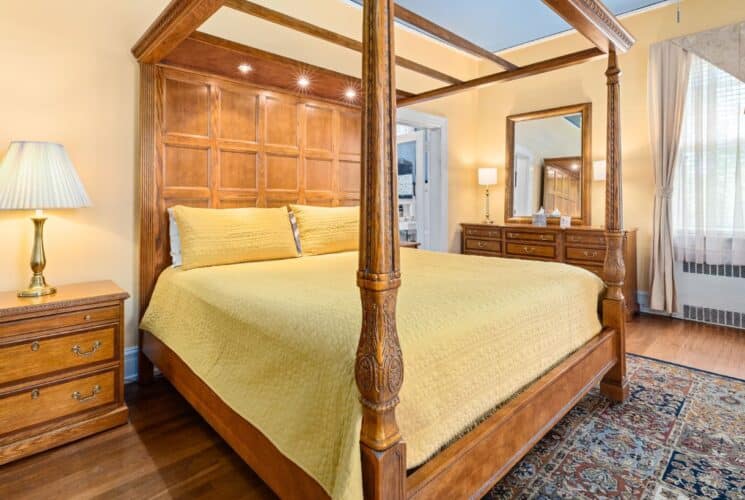 Bedroom with apricot walls, hardwood flooring, wooden four-poster canopy bed, yellow bedding, and wooden dresser