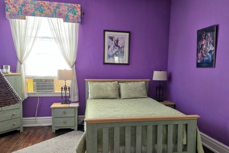 Bedroom with purple walls, hardwood flooring, wooden bed, light green bedding, and light green wooden dresser