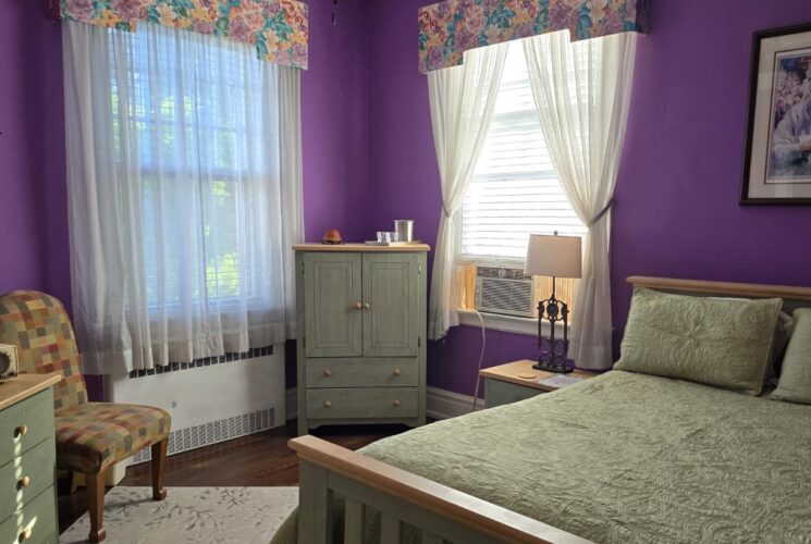 Bedroom with purple walls, hardwood flooring, wooden bed, light green bedding, and light green wooden dresser and cabinet