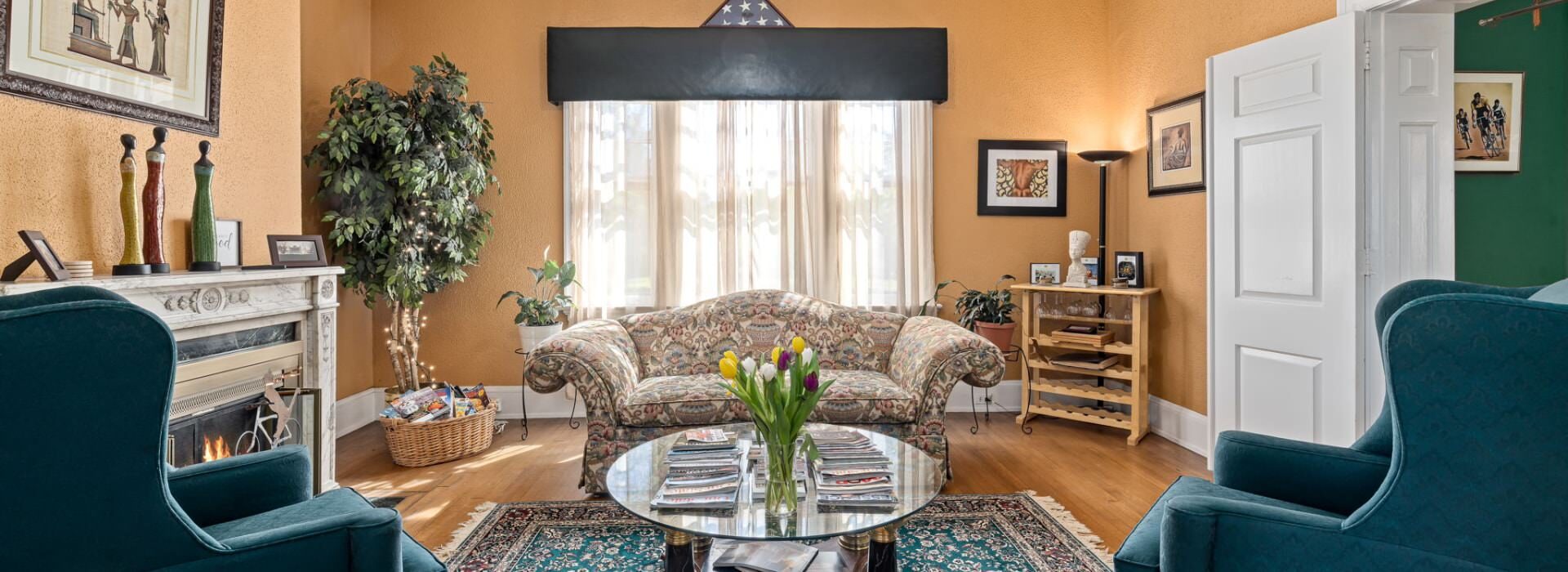 Dark cream walls, white trim, hardwood flooring, fireplace, upholstered sofa and armchairs, and large window