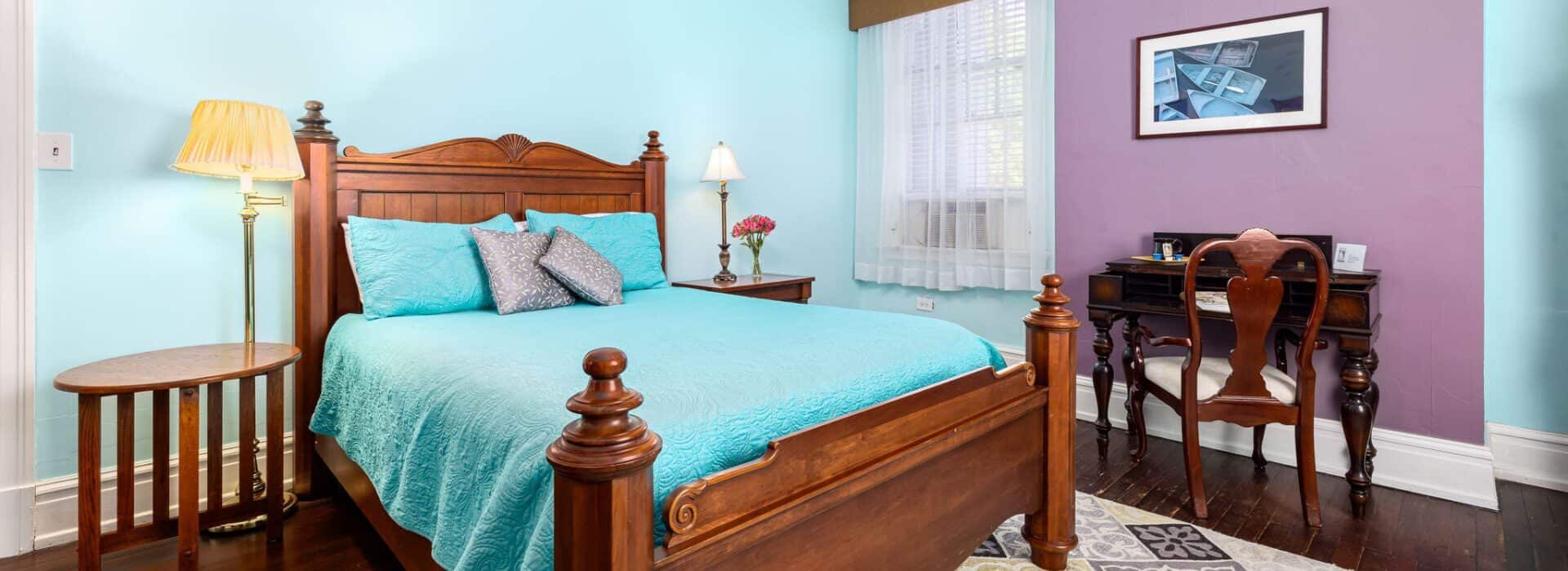 Bedroom with light blue and purple walls, hardwood flooring, wooden bed, turquoise bedding, and dark wooden antique desk