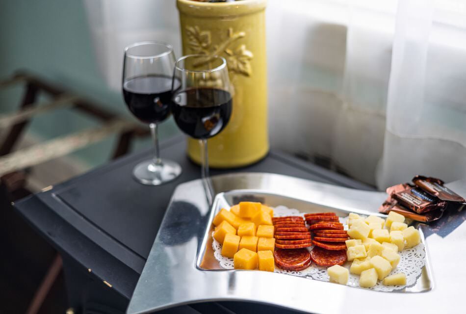 Close up view of silver tray with cheeses, sliced meat, and chocolates next to two glasses of red wine