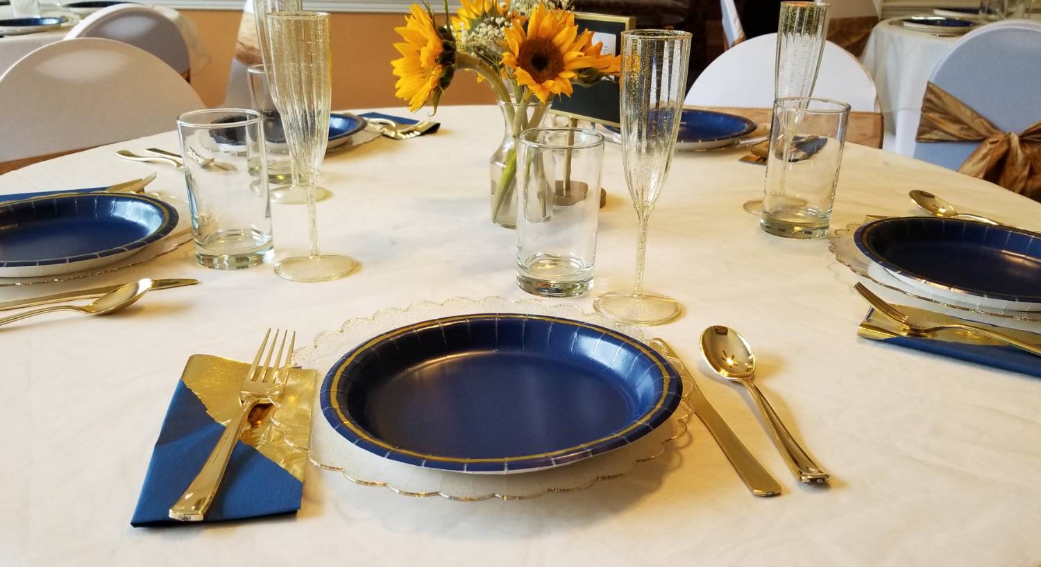 Close up view of round table with white tablecloth and blue and gold place settings around the table