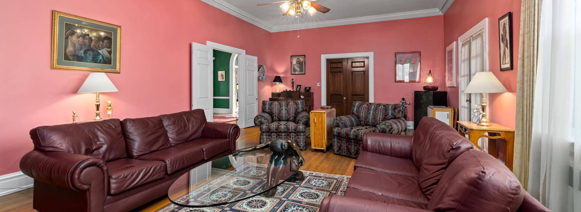 Living room with coral walls, hardwood flooring, brown leather sofas, multicolored upholstered recliners, and large windows