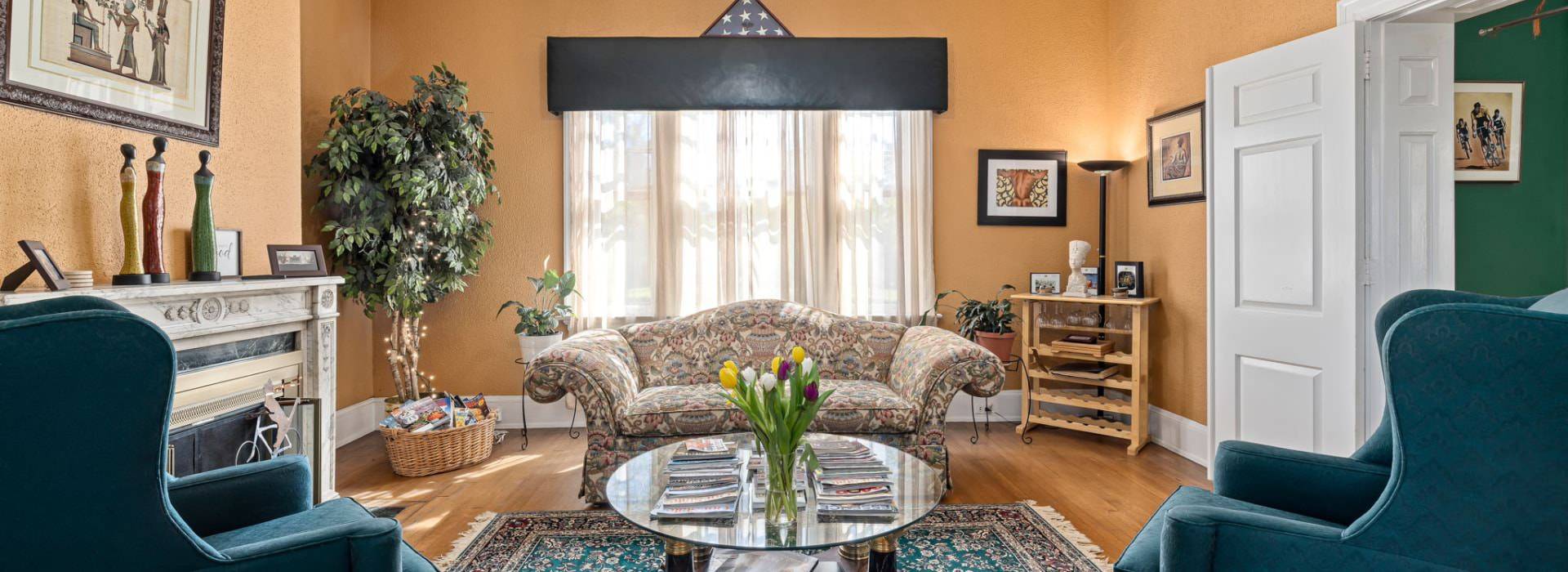 Dark cream walls, white trim, hardwood flooring, fireplace, upholstered sofa and armchairs, and large window