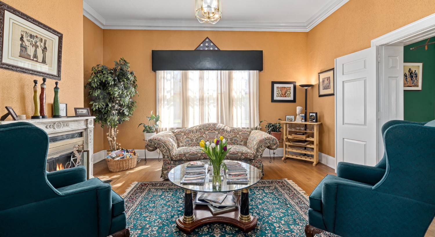 Dark cream walls, white trim, hardwood flooring, fireplace, upholstered sofa and armchairs, and large window