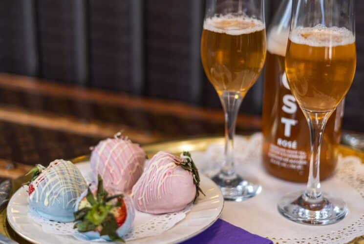 Close up view of blue and pink chocolate covered strawberries and two glasses filled with Rose